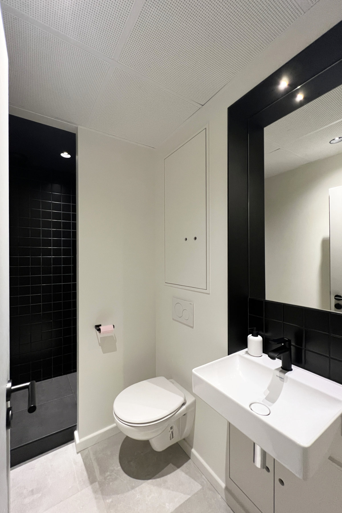 Salle d'eau noire et blanche au style épuré avec sanitaire et lavabo au premier plan